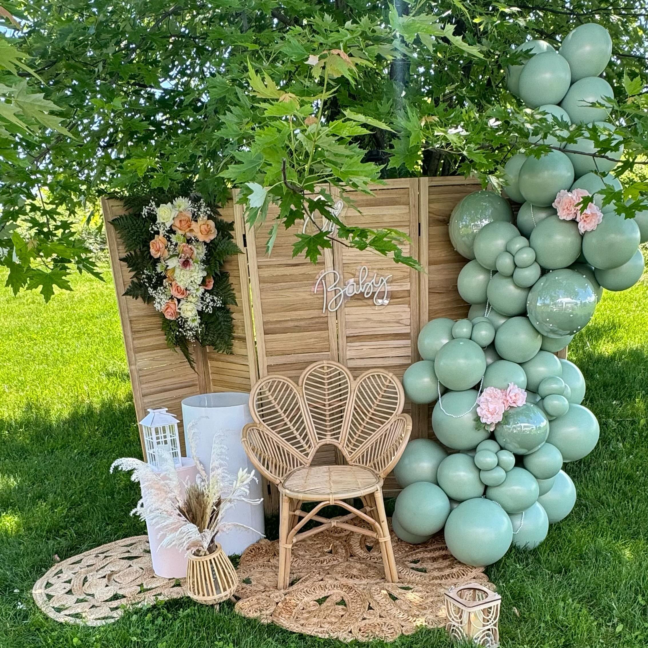 Signature sage green balloon garland install with boho rattan chair and floral accents